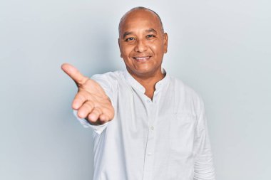 Orta yaşlı, sıradan kıyafetler giyen, dostça gülümseyen, selamlaşmak ve selamlamak için el sıkışan bir Latin. başarılı iş. 