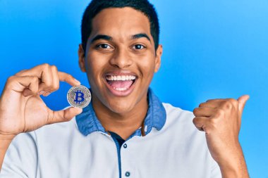 Genç, yakışıklı İspanyol adam elinde sanal para tutuyordu. Bitcoin parmağıyla yan tarafı gösteriyordu. Mutlulukla gülümsüyordu. 