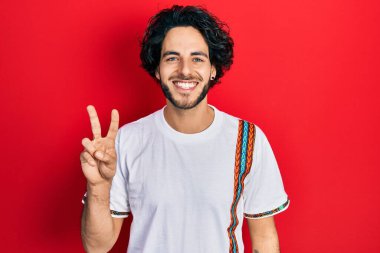 Yakışıklı, beyaz tişört giyen, kameraya gülümseyen ve zafer işareti yapan İspanyol bir adam. İki numara.. 