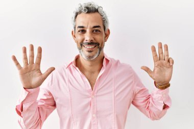 Orta yaşlı İspanyol bir adam tecrit edilmiş arka planda durup dokuz numarayı gösterirken kendinden emin ve mutlu bir şekilde gülümsüyor.. 