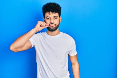 Sakallı, beyaz tişörtlü ağzı ve dudakları parmaklarıyla kapanan genç bir Arap. gizli ve sessiz, tabu konuşması 