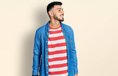 Sakallı, sıradan kot ceketli, yüzünde gülümsemeyle yan yana bakan genç İspanyol bir adam. Kendinden emin gülen. 