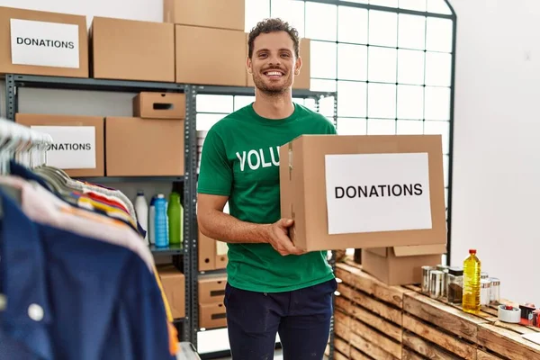 Gönüllü üniformalı genç İspanyol bir adam yardım merkezinde bağış kutusunu tutuyor.