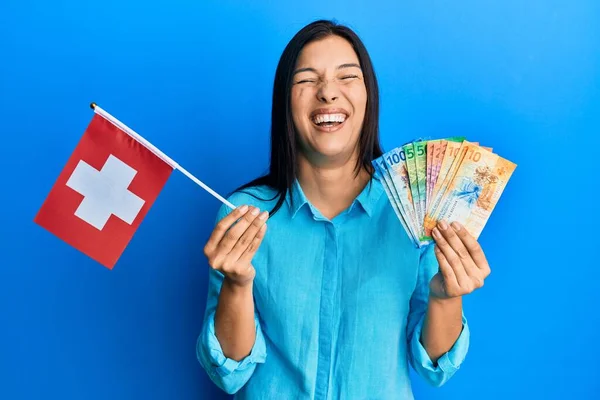 年轻的拉丁女人拿着天国国旗和法郎钞票 笑得很开心 笑得很大声 因为有一个可笑的疯狂笑话 — 图库照片