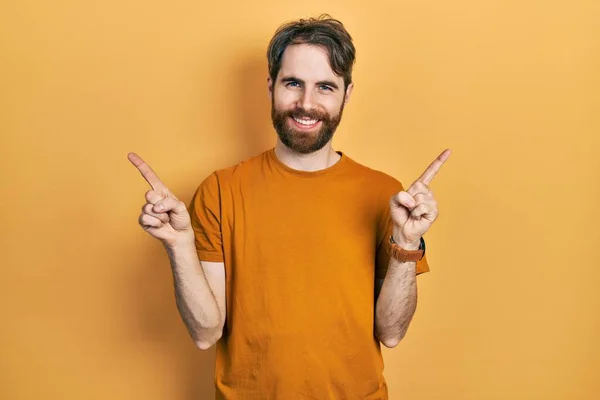 髭を生やした白人男性は 黄色のカジュアルなTシャツを着て さまざまな方向に指で自信を持って指して笑顔 広告のコピースペース — ストック写真