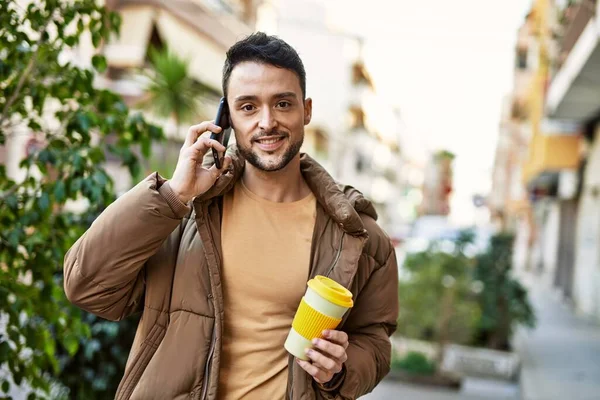 若いヒスパニック系の男が街のスマートフォンのコーヒーを飲んでいる — ストック写真