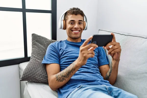 Young Hispanic Man Sitting Sofa Watching Video Smartphone Home — ストック写真