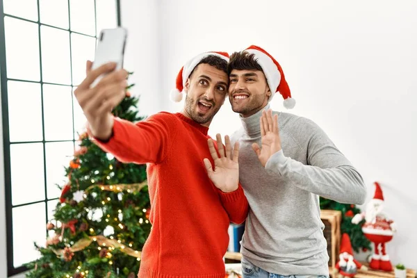 两只惊慌失措的男人在家里的圣诞树旁 用智能手机打着视频电话 — 图库照片