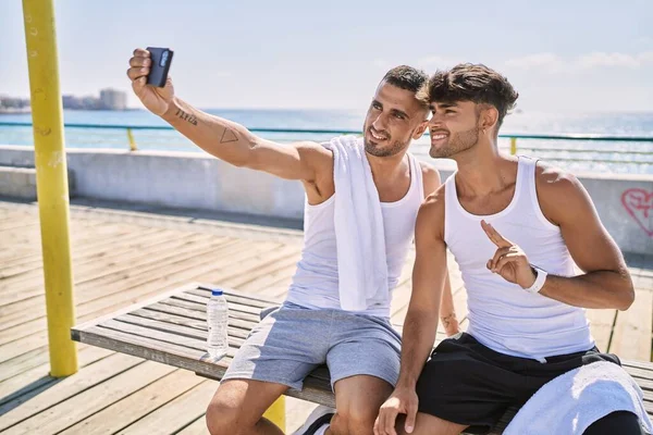 两只惊慌失措的男人坐在海滨的长椅上 靠智能手机自作主张 — 图库照片