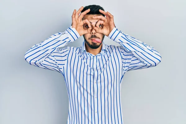 Sakallı, sıradan çizgili tişörtlü genç bir İspanyol dürbün gibi jest yapıyor, gözleri parmaklarından bakıyor. çılgın ifade. 