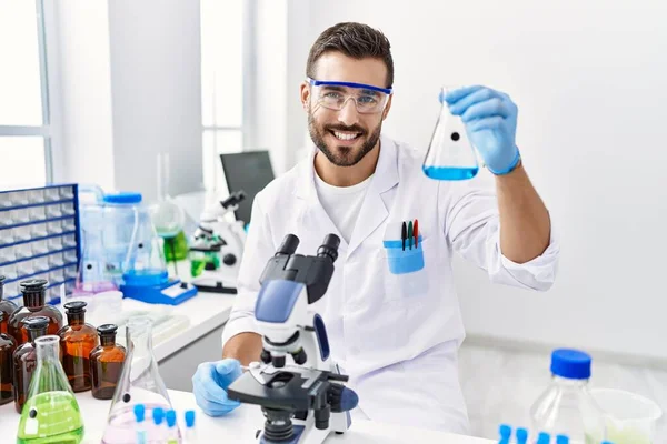 Laboratuvarda deney tüpü tutan bilim adamı üniforması giyen İspanyol genç adam.