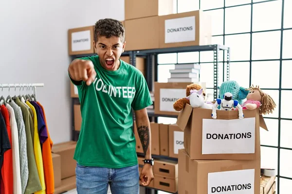 Young handsome hispanic man wearing volunteer t shirt at donations stand pointing displeased and frustrated to the camera, angry and furious with you
