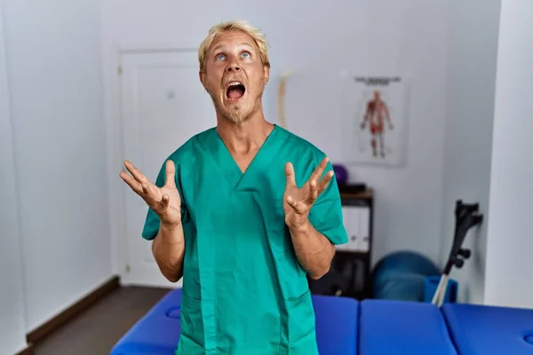 Jonge Blonde Man Draagt Fysiotherapeut Uniform Staan Kliniek Gek Gek — Stockfoto
