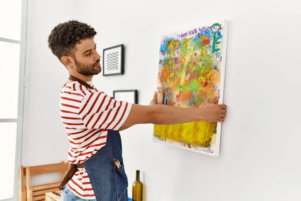 Genç Arap ressam mutlu bir şekilde gülümsüyor resim stüdyosunun duvarına resim çiziyor..