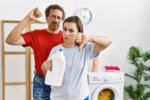 Międzyrasowa Para Średnim Wieku Robi Pranie Trzymając Butelkę Detergentach Rozgniewaną — Zdjęcie stockowe
