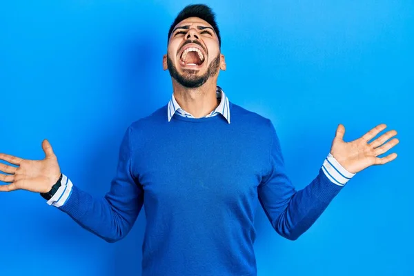 青いセーターを着た髭を生やした若いヒスパニック系の男は狂気と怒鳴り 積極的な表情と腕を上げて叫びました フラストレーションコンセプト — ストック写真