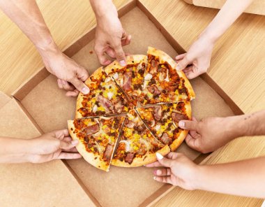 İtalyan pizzasının bir kısmını evdeki masada yiyen insanların elleri..