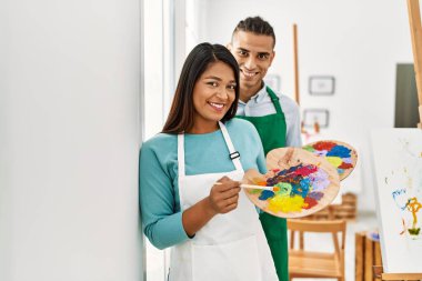 Genç Latin ressam çift gülümsüyor. Resim stüdyosunda fırça ve palet tutarken mutlu oluyorlar.