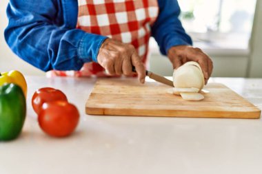 Kıdemli adam mutfakta soğan doğruyor.
