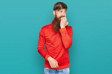 Uzun sakallı, günlük kıyafetler giyen, gergin görünen, elleri ağızdan tırnak yiyen kızıl saçlı bir adam. anksiyete. 