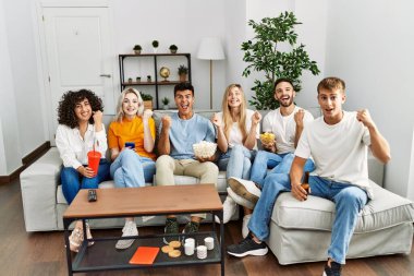 Bir grup insan kanepede oturmuş gururla bağırıyor zaferi kutluyor ve kollarını kaldırarak başarıyı kutluyor. 