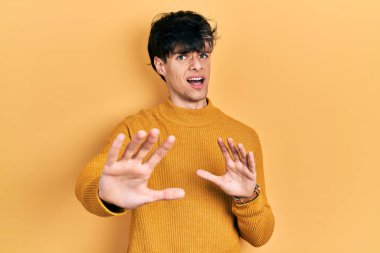 Yakışıklı hippi genç adam gündelik sarı süveter giyiyor. Korkudan dehşete düşmüş ve korkmuş. El hareketlerini bırak, şok içinde bağır. panik konsepti. 