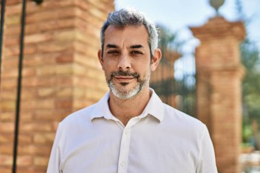 Orta yaşlı, kır saçlı, gülümseyen bir adam şehirde mutlu bir şekilde duruyor..