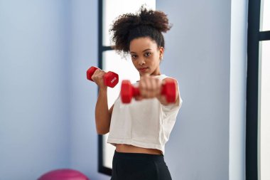Young african american woman boxing using dumbbells at sport center clipart