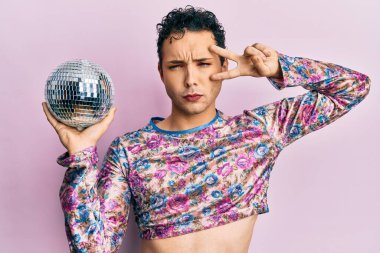 Parlak disko topunu kuşkucu ve gergin tutarak makyaj yapan yakışıklı bir adam sorun yüzünden somurtuyor. negatif kişi. 