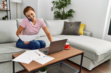 Akıllı telefondan konuşan ve evde çalışan genç bir kadın.