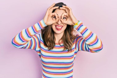 Günlük kıyafetler giyen genç İspanyol kız dürbün gibi jest yapıyor, gözleri parmaklarından bakıyor. çılgın ifade. 