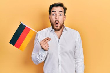 Handsome caucasian man with beard holding germany flag scared and amazed with open mouth for surprise, disbelief face 