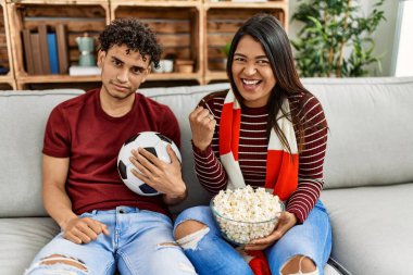 Evdeki kanepede oturan genç latin çift futbol maçını izliyor ve destekliyor..