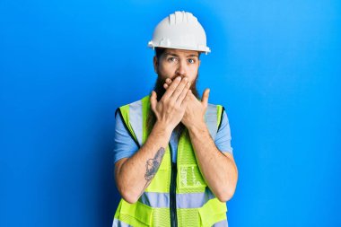 Uzun sakallı, güvenlik kaskı takan ve yansıtıcı ceket giyen kızıl saçlı adam yanlışlıkla ağzı ellerle kapatmış. gizli kavram. 