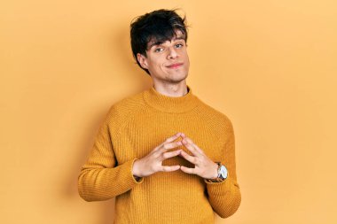 Yakışıklı hippi genç adam sıradan sarı süveter giyen elleri ve parmakları çapraz gülümseyerek gevşemiş ve neşeli. Başarı ve iyimserlik 