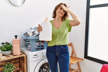 Çamaşır yıkayan orta yaşlı kadın elinde deterjan şişesi tutarken gergin ve hayal kırıklığına uğramış, şaşırmış ve sinirli bir yüz ifadesi vardı. 