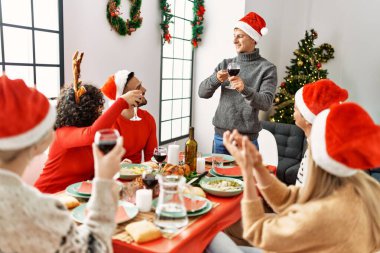 Mutlu bir şekilde gülümseyen bir grup genç Noel yemeği yiyor ve evde kadeh kaldırıyor..