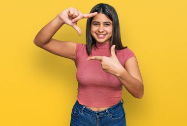 Gündelik tişört giyen genç İspanyol kız gülümseyerek elleri ve parmakları gülen yüzle çerçeve yapıyor. yaratıcılık ve fotoğrafçılık kavramı. 