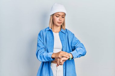 Yün şapka takan güzel sarışın kadın kol saatini kontrol ediyor, rahat ve kendinden emin. 