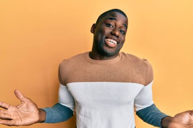 Sıradan kıyafetler giyen, kafası karışmış, elleri ve kolları havada genç Afro-Amerikalı bir adam. şüphe kavramı. 