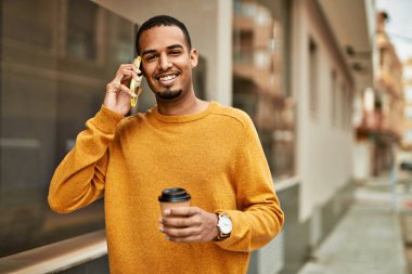 Genç Afrikalı Amerikalı adam akıllı telefonda konuşuyor. Şehirde kahve içiyor..