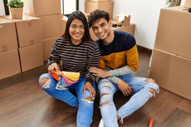 Young latin couple choosing paint color sitting on the floor at new home.