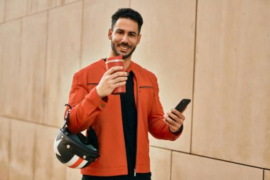 Genç İspanyol adam akıllı telefon kullanıyor. Şehirde kahve kaskı içiyor..