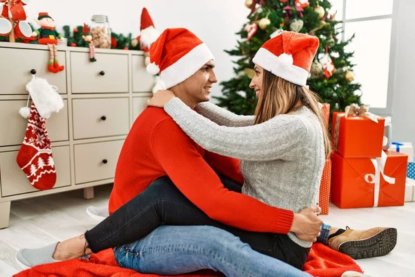 Młoda Para Uśmiechnięta Szczęśliwa Świątecznym Kapeluszu Siedząc Podłodze Przytulając Się — Zdjęcie stockowe