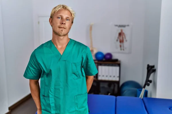 Klinikte Dikilen Fizyoterapist Üniforması Giyen Genç Sarışın Adam Yüzünde Ciddi — Stok fotoğraf