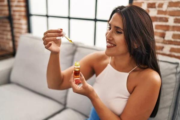 Young hispanic woman drinking syrup sitting on sofa at home