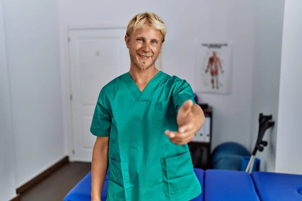 Jonge Blonde Man Draagt Fysiotherapeut Uniform Staan Kliniek Glimlachend Vriendelijk — Stockfoto