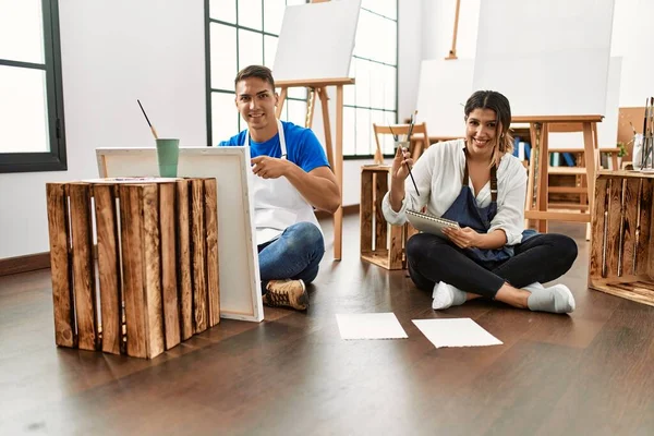 Sanat stüdyosundaki genç İspanyol çift mutlu bir şekilde el ve parmak işareti yapıyor. 