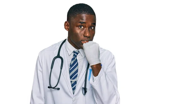 医師の制服と聴診器を身に着けている若いアフリカ系アメリカ人の男性は 口の爪をかむ上で手で強調し 緊張している 不安の問題 — ストック写真