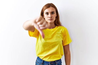 Young brunette woman standing over isolated background looking unhappy and angry showing rejection and negative with thumbs down gesture. bad expression. 